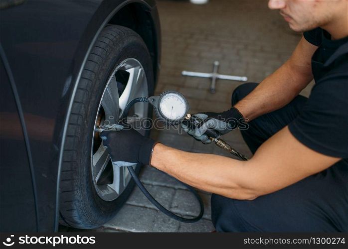 Auto mechanic checks the tire pressure in repairing service. Man repairs car tyre in garage, professional automobile inspection in workshop. Auto mechanic checks the tire pressure in service