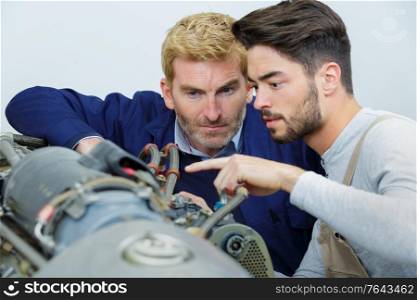 auto mechanic fixing a machine with apprentice