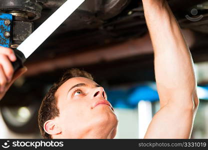 Auto mechanic in his workshop looking under a car on a hoist