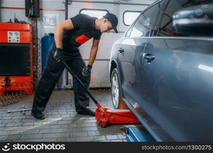 Auto mechanic jacks the car in tire service. Technician repairs car tyre in garage, professional automobile inspection in workshop, repairman
