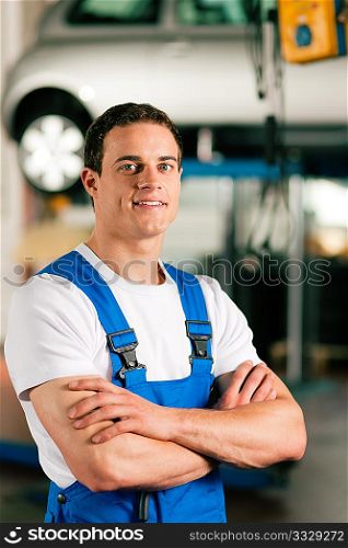 Auto mechanic standing in his workshop in front of a car on a hoist