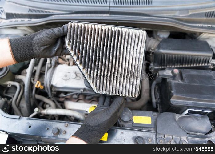 Auto mechanic wearing protective work gloves holding dirty air filter above a car engine