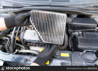 Auto mechanic wearing protective work gloves holding dirty air filter above a car engine