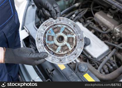 Auto mechanic wearing protective work gloves holding old clutch disc over a car engine