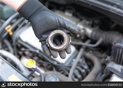 Auto mechanic wearing protective work gloves holding old clutch release bearing over a car engine