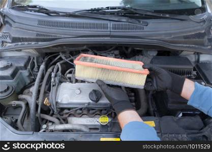 Auto mechanic wearing protective work gloves holding used air filter above a car engine