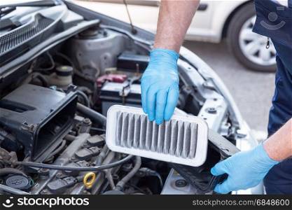 Auto mechanic wearing protective work gloves holds a dirty air filter over a car engine. Internal combustion engine air filter.