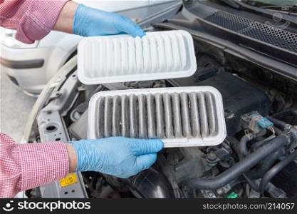 Auto mechanic wearing protective work gloves holds dirty and clean air filters over a car engine