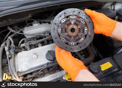 Auto mechanic wearing protective work gloves holds old clutch disc above a car engine
