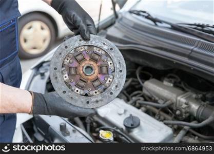 Auto mechanic wearing protective work gloves holds old clutch disc over a car engine