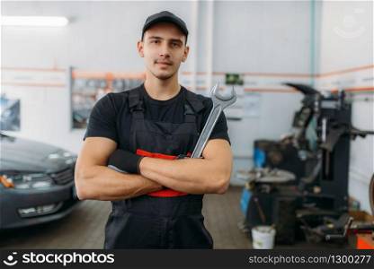 Auto mechanic with wrench, tire service industry or business. Technician repairs car tyre in garage, professional automobile inspection in workshop, repairman job