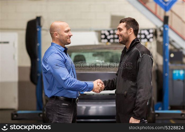 auto service, repair, deal and people concept - mechanic and customer or car owner shaking hands at workshop. mechanic and customer shaking hands at car service