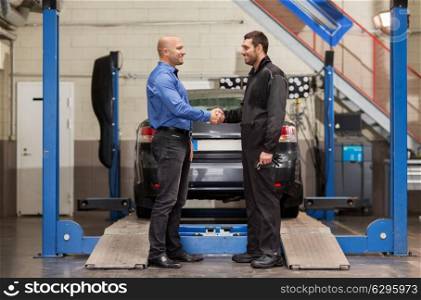 auto service, repair, deal and people concept - mechanic and customer or car owner shaking hands at workshop. mechanic and customer shaking hands at car service