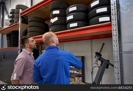 auto service, repair, maintenance and people concept - mechanic and man looking at tires at car shop