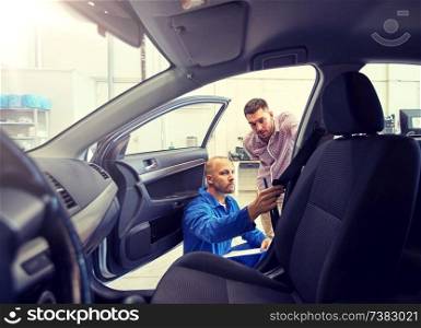 auto service, repair, maintenance and people concept - mechanic checking car seat belt with man or owner at workshop. mechanic and man checking seat belt at car shop