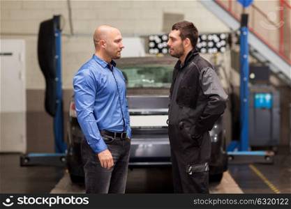auto service, repair, maintenance and people concept - mechanic talking to customer or car owner at workshop. auto mechanic talking to customer at car shop
