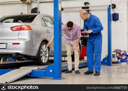 auto service, repair, maintenance and people concept - mechanic with clipboard and man or owner showing wheel at car shop