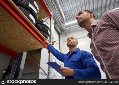 auto service, repair, maintenance and people concept - mechanic with clipboard and man looking at tires at car shop