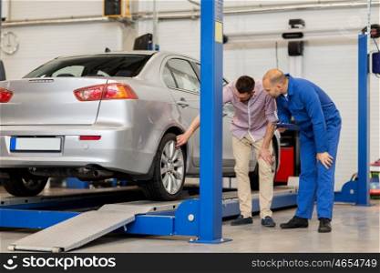 auto service, repair, maintenance and people concept - mechanic with clipboard and man or owner showing wheel at car shop