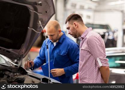 auto service, repair, maintenance and people concept - mechanic with clipboard and man or owner looking at broken car at shop. auto mechanic with clipboard and man at car shop