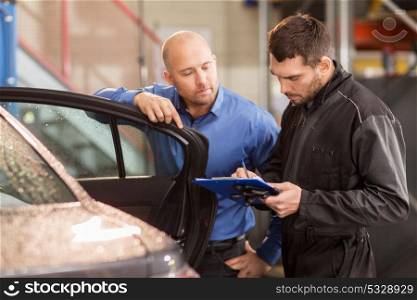 auto service, repair, maintenance and people concept - mechanic with clipboard and customer or car owner at workshop. auto mechanic and customer at car shop
