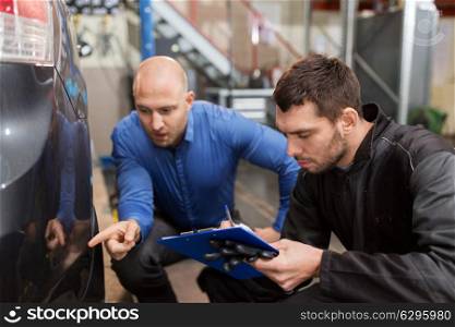 auto service, repair, maintenance and people concept - mechanic with clipboard and customer or owner pointing finger to car at workshop. auto mechanic and customer looking at car
