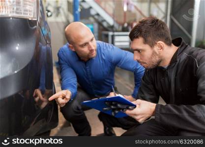 auto service, repair, maintenance and people concept - mechanic with clipboard and customer or owner pointing finger to car at workshop. auto mechanic and customer looking at car