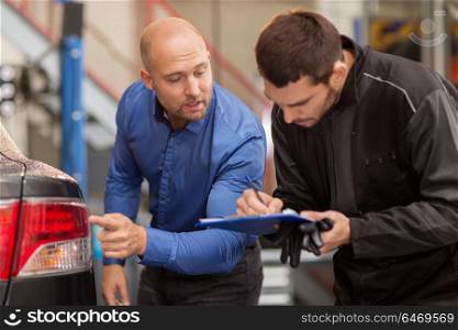 auto service, repair, maintenance and people concept - mechanic with clipboard and customer or car owner looking at taillight at workshop. mechanic and customer looking at car taillight