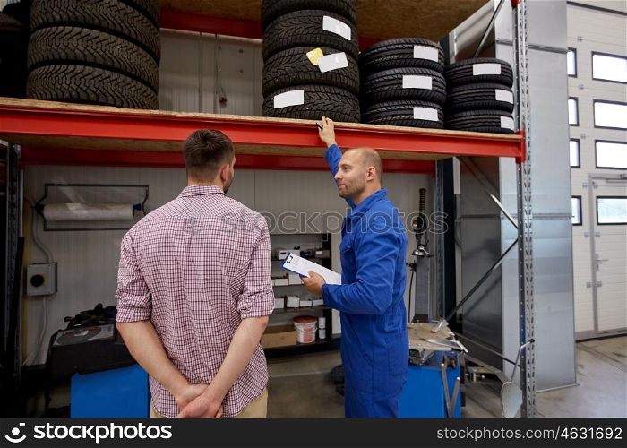 auto service, repair, maintenance and people concept - mechanic with clipboard showing tire to man at car shop