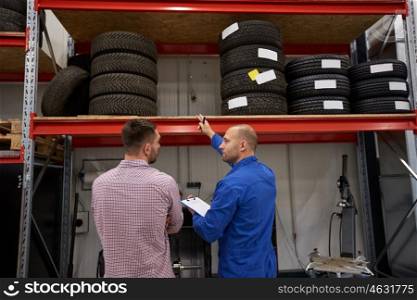 auto service, repair, maintenance and people concept - mechanic with clipboard showing tire to man at car shop