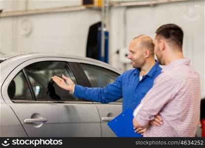 auto service, repair, maintenance and people concept - mechanic with clipboard showing side window to man or owner at car shop