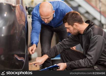 auto service, repair, maintenance and people concept - mechanic with clipboard showing tire to customer or car owner at workshop. auto mechanic and customer looking at car tire