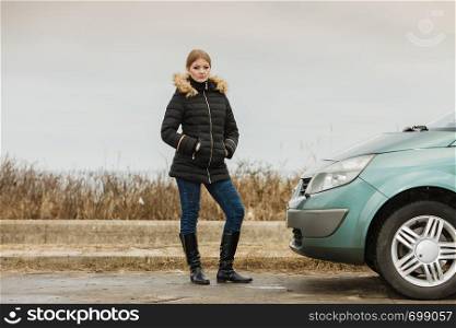 Auto traveling concept. Blonde driver woman in winter clothes standing next to her car.. Blonde driver woman standing next to car