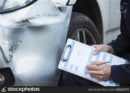 Auto Workshop Mechanic Inspecting Damage To Car And Filling In Repair Estimate