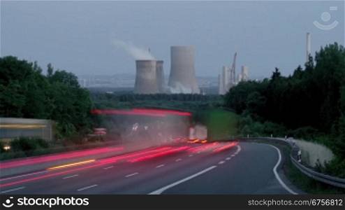 Autobahn mit fliessendem Verkehr vor Kraftwerk. Totale bei Abendstimmung. Im Hintergrund eine Kohlekraftwerk mit Baustelle einer Kraftwerkserweiterung.