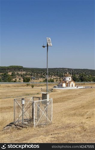 Automated weather station in a field with a church in the background, near Monforte, Portugal