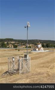 Automated weather station in a field with a church in the background, near Monforte, Portugal