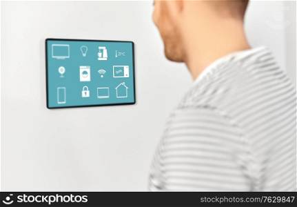 automation, internet of things and technology concept - close up of happy smiling man looking at tablet pc computer on wall with menu icons on screen at smart home. happy man looking at tablet computer at smart home