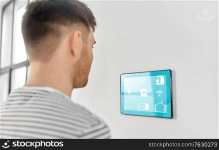 automation, internet of things and technology concept - man looking at tablet pc computer with smart home icons on wall. man looking at tablet computer at smart home