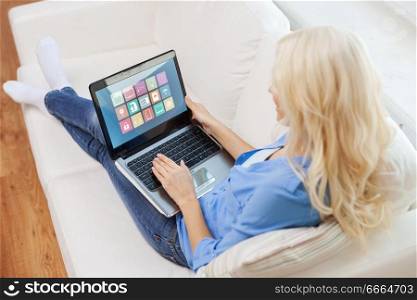 automation, internet of things and technology concept - woman with smart home icons on laptop computer screen sitting on sofa. woman with smart home icons on laptop computer