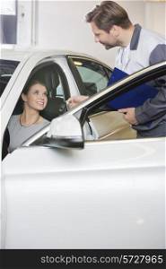 Automobile mechanic giving car key to female customer in repair shop