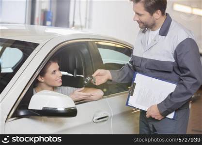 Automobile mechanic giving car key to female customer in workshop