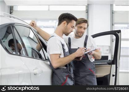 Automobile mechanics checking checklist while standing by car in workshop