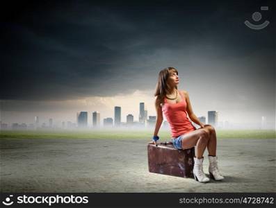 Autostop travel. Young pretty girl traveler sitting on suitcase aside of road