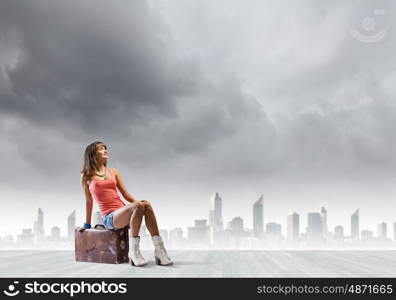 Autostop travel. Young pretty girl traveler sitting on suitcase aside of road