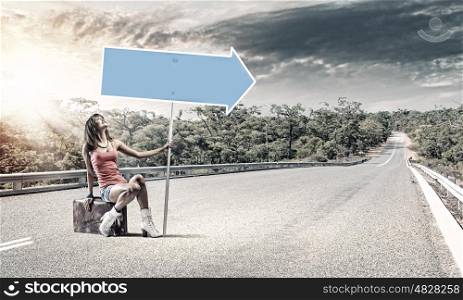 Autostop traveling. Young pretty girl traveler sitting on suitcase aside of road