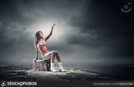 Autostop traveling. Young pretty girl traveler sitting on suitcase aside of road