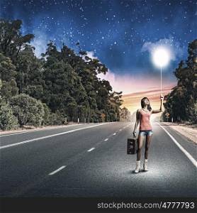 Autostop traveling. Young pretty woman tourist with suitcase walking on road