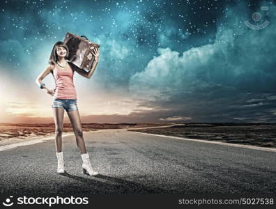 Autostop traveling. Young pretty woman tourist with suitcase walking on road