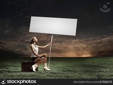 Autostop traveling. Young woman with blank banner sitting on suitcase